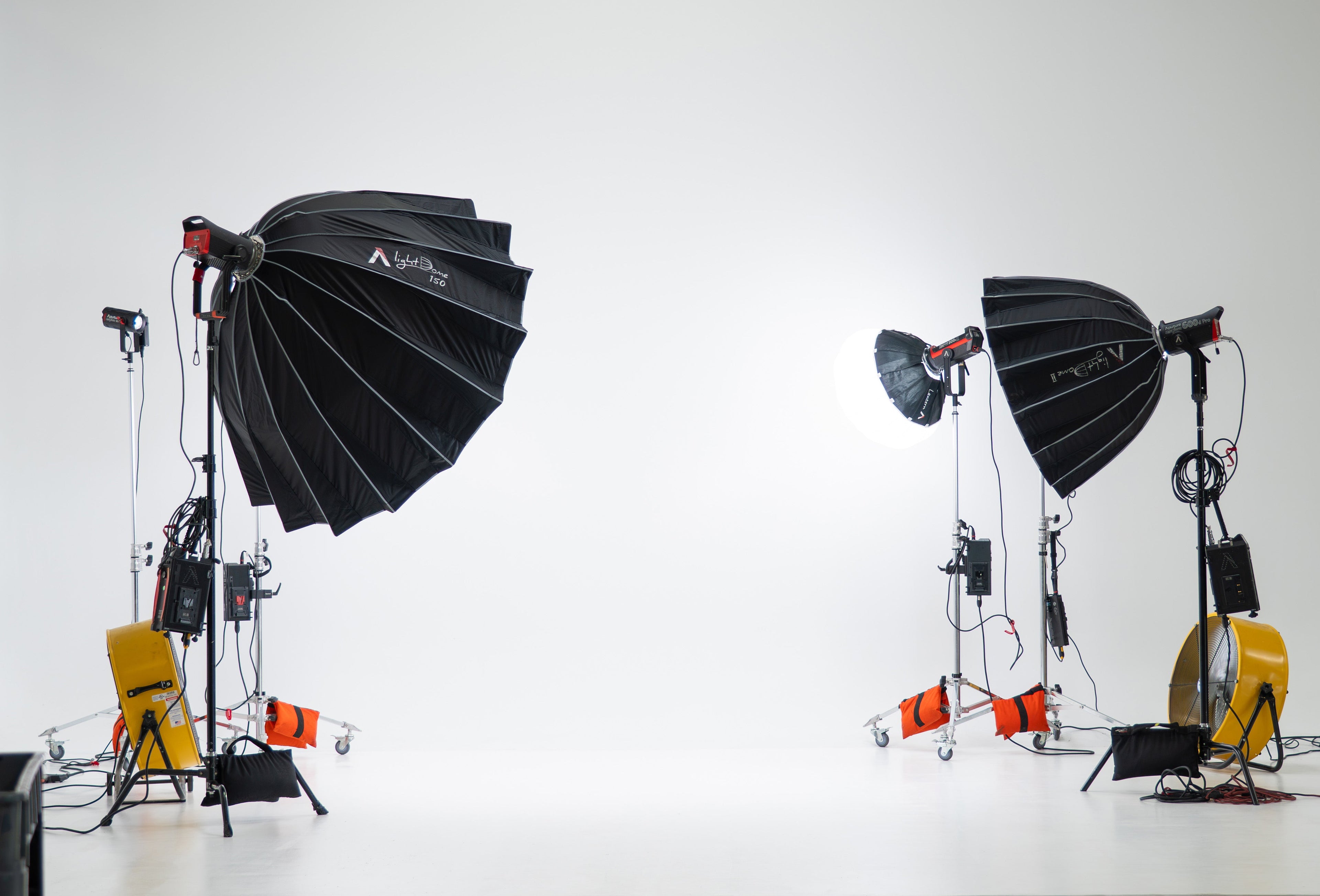 Studio lighting equipment with softboxes and stands against a white wall.